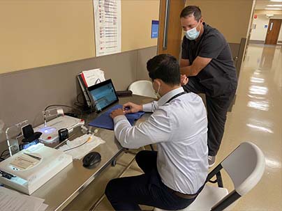educator guiding doctor at a desk on using the ETOSS system as the doctor moves a guidewire through a simulated vessel on the laptop screen